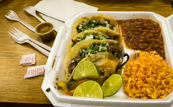 Three tacos with rice and beans in a styrofoam container.
